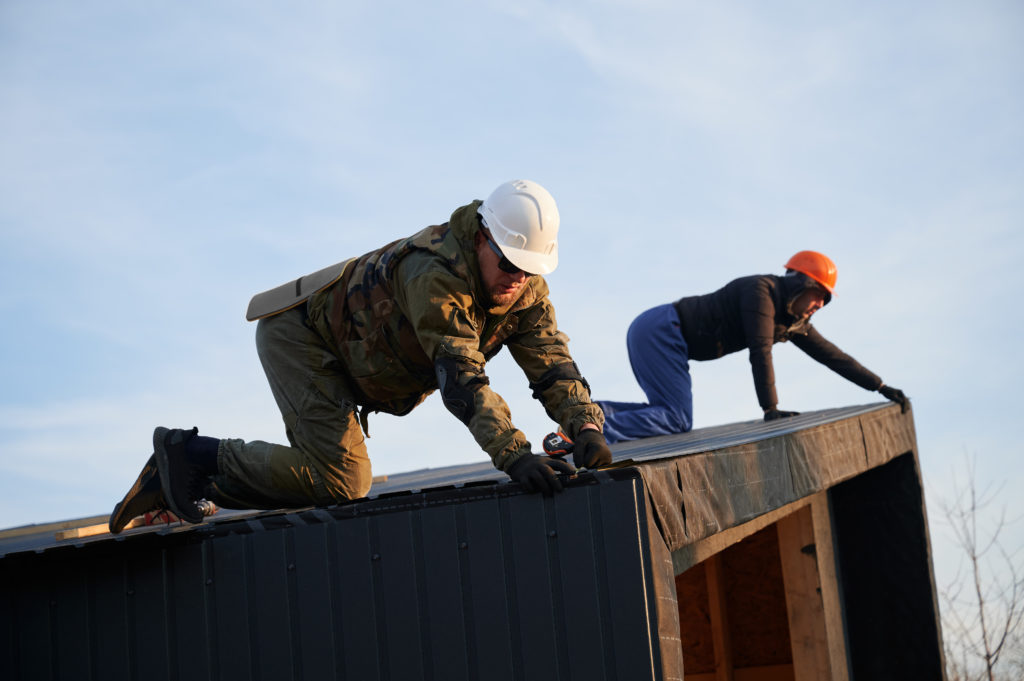 Builder installing corrugated iron sheet used as facade of future wooden frame house.