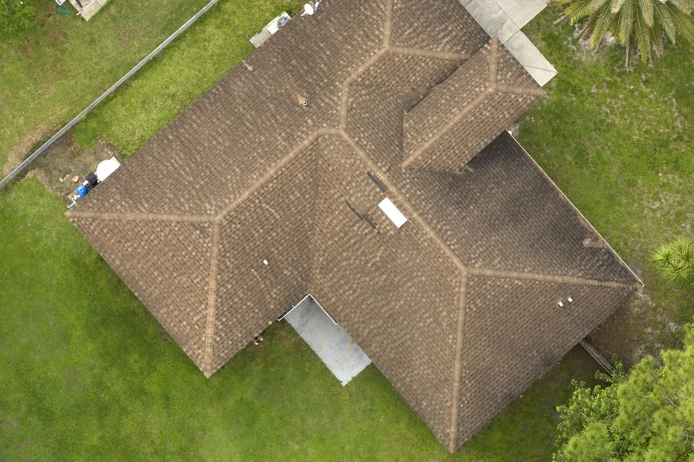 Aerial view of typical contemporary american private house with roof top covered with asphalt shingles and green lawn on yard.