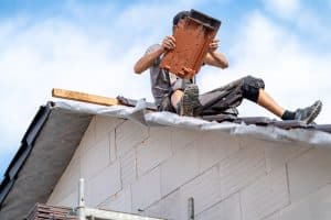 roofer with ceramic tile in hand on roof of house.