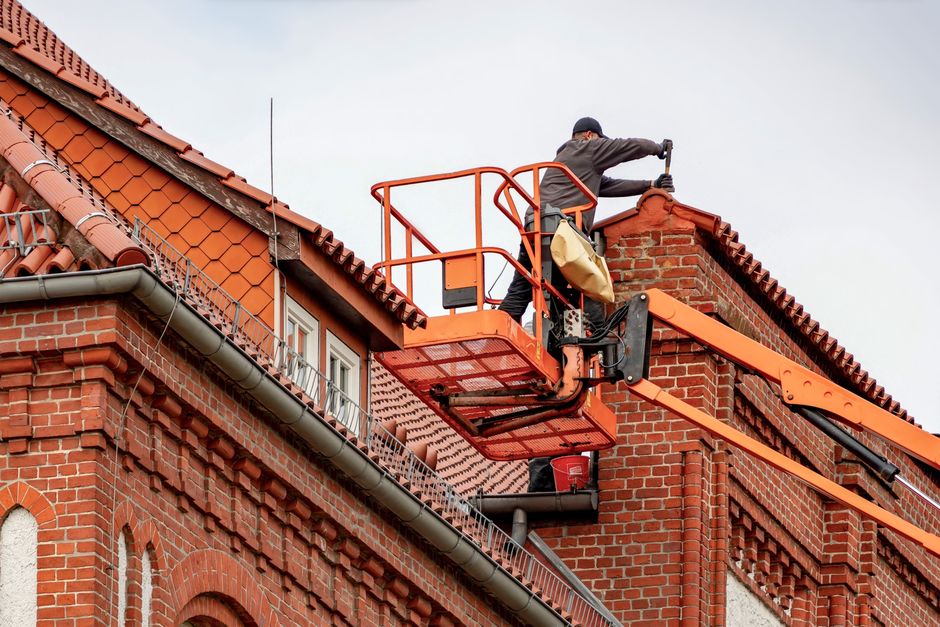 Contractor inspecting fascia board and gutter attachment on a roof edge